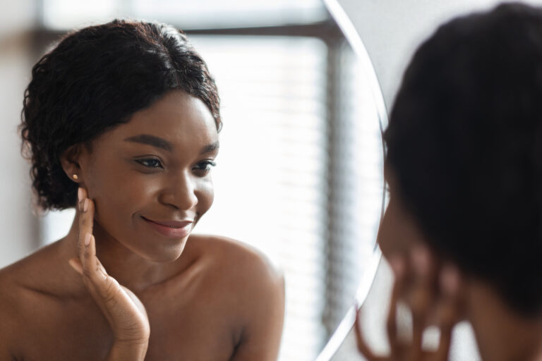 Mirror reflection of pretty black woman applying facial product