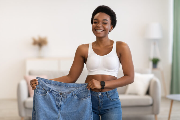 Skinny Black Female Showing Old Large Jeans After Weight-Loss Indoor